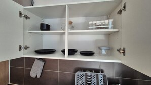 Une cuisine avec des meubles blancs, des assiettes noires, une bouilloire, des pots à épices et un manique suspendu.