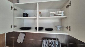 A kitchen with white cabinets, black plates, a kettle, spice jars, and a hanging oven mitt. - Wildstein-Ferienwohnungen- Rote Wand (Bayrischzell)