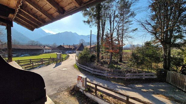 Une route de campagne menant à un village avec des maisons et une chaîne de montagnes en arrière-plan.