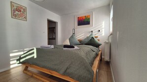 Une chambre à coucher avec un lit, des oreillers, un radiateur, une porte et un tableau au mur.