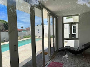 A room with a large sliding glass door leading to a pool area, a hammock, and a patterned floor. - Cosy & Tranquil Family Beach Getaway (Gqeberha)
