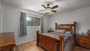 A bedroom with a wooden bed, a ceiling fan, a window with curtains, a bedside table, and a nightstand. - Riverkern Retreat House (Kernville)