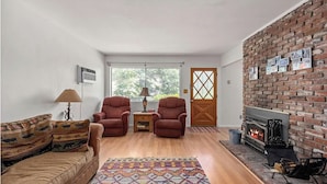 A living room with a fireplace, two armchairs, a sofa, a patterned rug, and a door with a window view. - Riverkern Retreat House (Kernville)