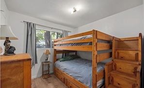 Una cama individual con estructura de madera, una mesita de noche con lámpara, y una ventana con cortinas.