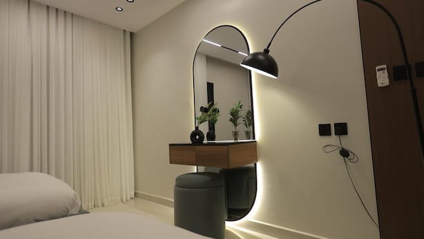 Habitació d'hotel moderna amb un llit, una taula de nit, un mirall, una làmpada i un petit safataire.