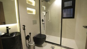 Un bany modern amb un rentaplat amb acabats negres, un vàter negre, una dutxa amb porta de vidre i un mirall amb il·luminació.