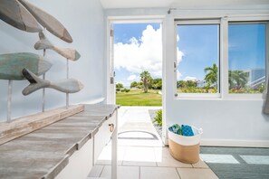 Ein Zimmer mit einer Holzbank, einem Korb und Blick durch eine Glastür auf eine Rasenfläche.