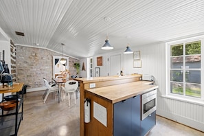 A kitchen with a wooden island, white walls, and a stone accent wall. - 2 Blocks 2 Main | Cowboy Pool | Hot Tub | Fire Pit (Fredericksburg)