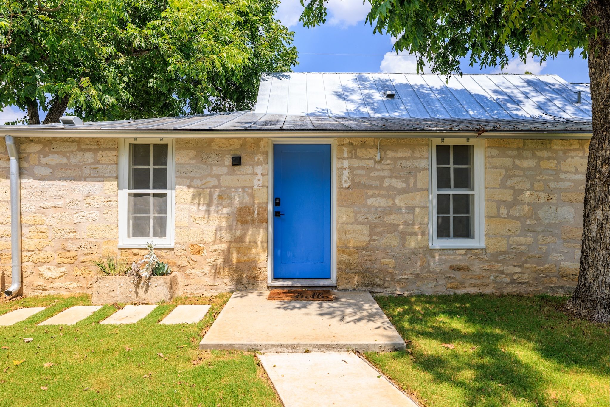 A stone building with a blue door, two windows, and a metal roof.