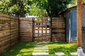 A wooden gate with a grid pattern, a grassy area with stepping stones, and a blue building. - Pool&Hot Tub | Large Yard | Walk2Main | Fire Pit (Fredericksburg)