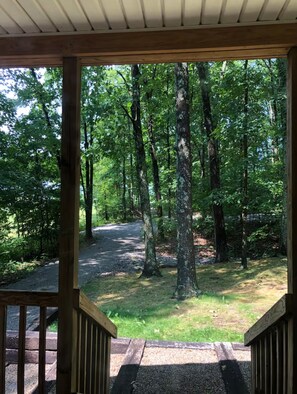 A covered wooden deck with a view of a forested area and a gravel path. - “Serenity Now” a 2BR country home in the heart of Amish Country (West Union)