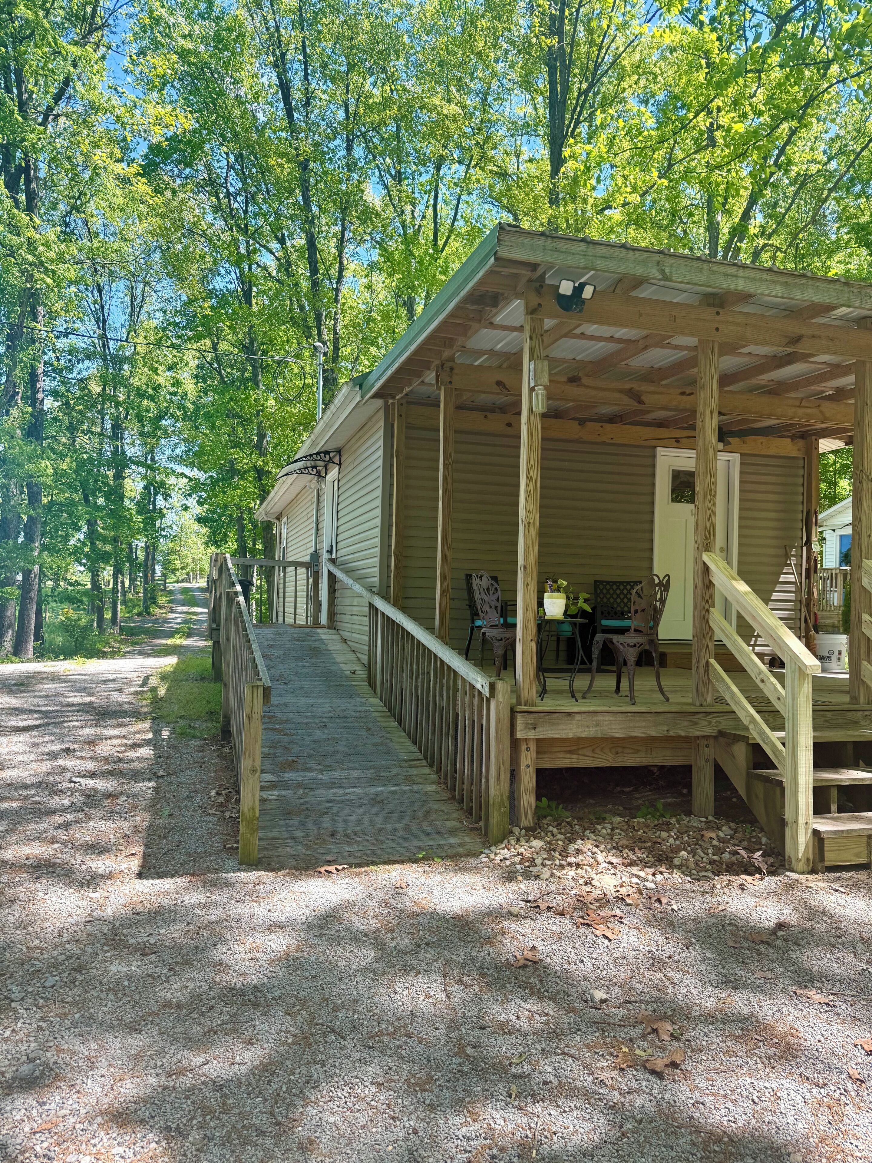 A wooden cabin with a porch, a table with chairs, and a gravel path leading to it.