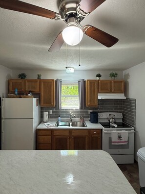 A kitchen with wooden cabinets, a white refrigerator, a sink, a stove, and a ceiling fan.