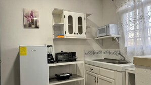 Eine kleine Küche mit weißen Schränken, einer Mikrowelle, einer Kaffeemaschine und einem Kühlschrank.