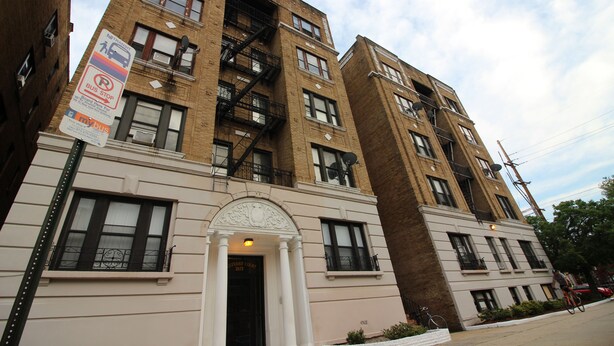 A multi-story building with a prominent entrance, fire escapes, and a sign indicating a bus stop.