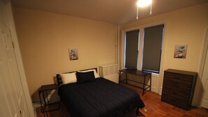 A bedroom with a bed, a desk, a dresser, and a window.