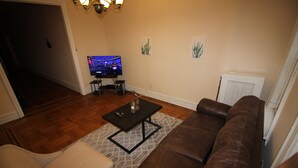 A living room with a brown leather couch, a beige armchair, a black coffee table, and a flat-screen TV on a stand.
