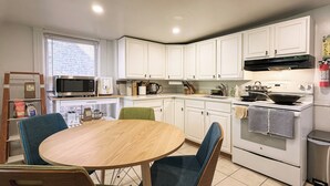 A modern kitchen with white cabinets, a microwave, a stove, and a dining table with chairs. - The Quaint House: Modern Heritage in Roundout Kingston Waterfront (Kingston)
