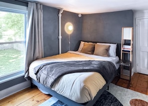 A bedroom with a bed, a bedside table, a lamp, a window with curtains, and a view of the outdoors. - The Quaint House: Modern Heritage in Roundout Kingston Waterfront (Kingston)