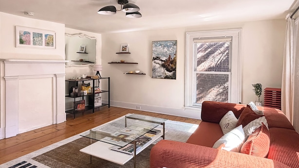 A living room with a fireplace, a glass coffee table, a red sofa, and a large window with a view of a brick wall. - The Quaint House: Modern Heritage in Roundout Kingston Waterfront (Kingston)