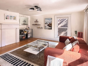 A living room with a fireplace, a glass coffee table, a red sofa, and a large window with a view of a brick wall. - The Quaint House: Modern Heritage in Roundout Kingston Waterfront (Kingston)