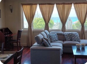 Ein Wohnzimmer mit einer Couch, einem Esstisch und Meerblick durch große Fenster.