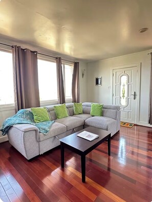 Ein Wohnzimmer mit grauem Ecksofa, einem schwarzen Couchtisch und Holzboden.