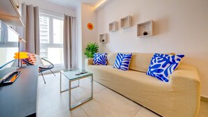 A modern living room with a sofa, a glass coffee table, a potted plant, and a wall-mounted clock. - 2BR Apt in St Julian’s Heart (St. Julian`s)