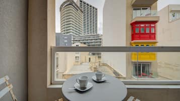 Ein Balkon mit Tisch und Stühlen, ein Fenster mit Blick auf eine Stadtlandschaft und Gebäude.