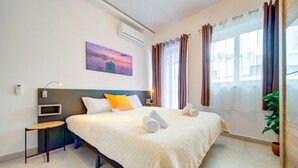 A hotel room with a bed, bedside table, air conditioning unit, window with curtains, and a painting on the wall. - 2BR Apt in St Julian’s Heart (St. Julian`s)