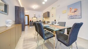 A modern dining area with a glass table, woven chairs, a clock, and a painting of a flamingo. - 2BR Apt in St Julian’s Heart (St. Julian`s)