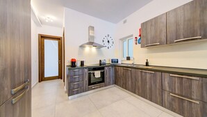 A modern kitchen with wooden cabinets, a built-in oven, a microwave, and a clock on the wall. - 2BR Apt in St Julian’s Heart (St. Julian`s)