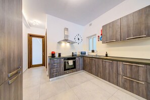 A modern kitchen with wooden cabinets, a built-in oven, a microwave, and a clock on the wall. - 2BR Apt in St Julian’s Heart (St. Julian`s)
