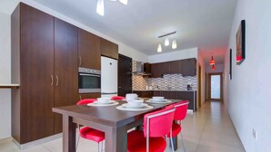 Une cuisine moderne avec des meubles en bois foncé, une table à manger avec des chaises rouges et un mur recouvert de carreaux.