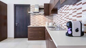 Une cuisine moderne avec des meubles de couleur sombre en bois, un pare-feu en carreaux et une machine à café posée sur le plan de travail.