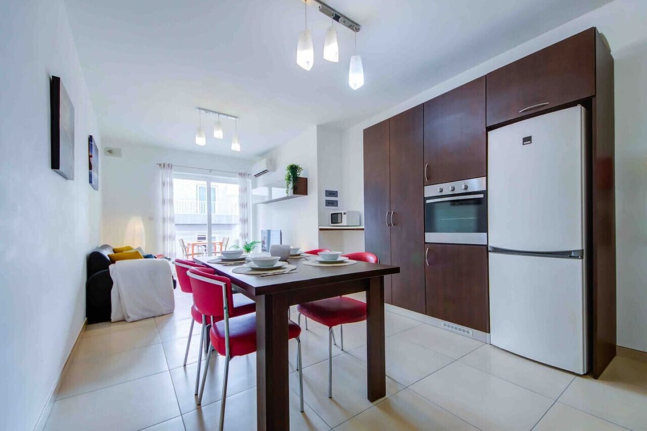A modern kitchen with a dining table, chairs, and a refrigerator.