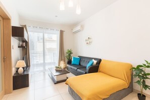 A modern room with a sofa, a bed, a coffee table, a lamp, a plant, and a view through a window. - Best of St. Julian’s: Prime Location in Paceville (San Ġiljan)