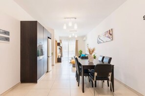 A modern kitchen with dark cabinetry, a dining area with a table and chairs, and a hallway leading to a living space. - Best of St. Julian’s: Prime Location in Paceville (San Ġiljan)