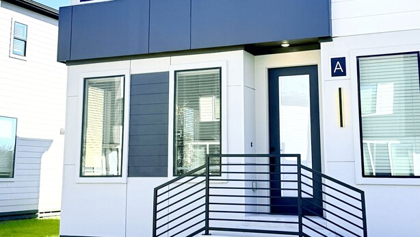 A modern two-story building with a flat roof, large windows, and a staircase with a metal railing. - Modern 2BR Townhome - King + Queen - 20 Min to Downtown, IAH, & IAH - Gated (Houston)