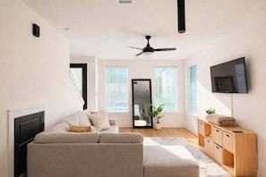 Ein modernes Wohnzimmer mit einer Couch, einem Fernseher, einem Deckenventilator und einem Holzschrank.
