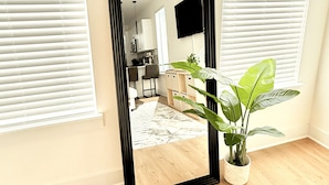 A room with a large mirror, a potted plant, and a view into a kitchen area. - Modern 2BR Townhome - King + Queen - 20 Min to Downtown, IAH, & IAH - Gated (Houston)