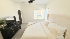 A bedroom with a bed, a TV on a dresser, a ceiling fan, and a window with blinds. - Modern 2BR Townhome - King + Queen - 20 Min to Downtown, IAH, & IAH - Gated (Houston)