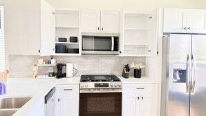 A modern kitchen with white cabinets, a stainless steel refrigerator, a microwave, a stove, and a dishwasher. - Modern 2BR Townhome - King + Queen - 20 Min to Downtown, IAH, & IAH - Gated (Houston)