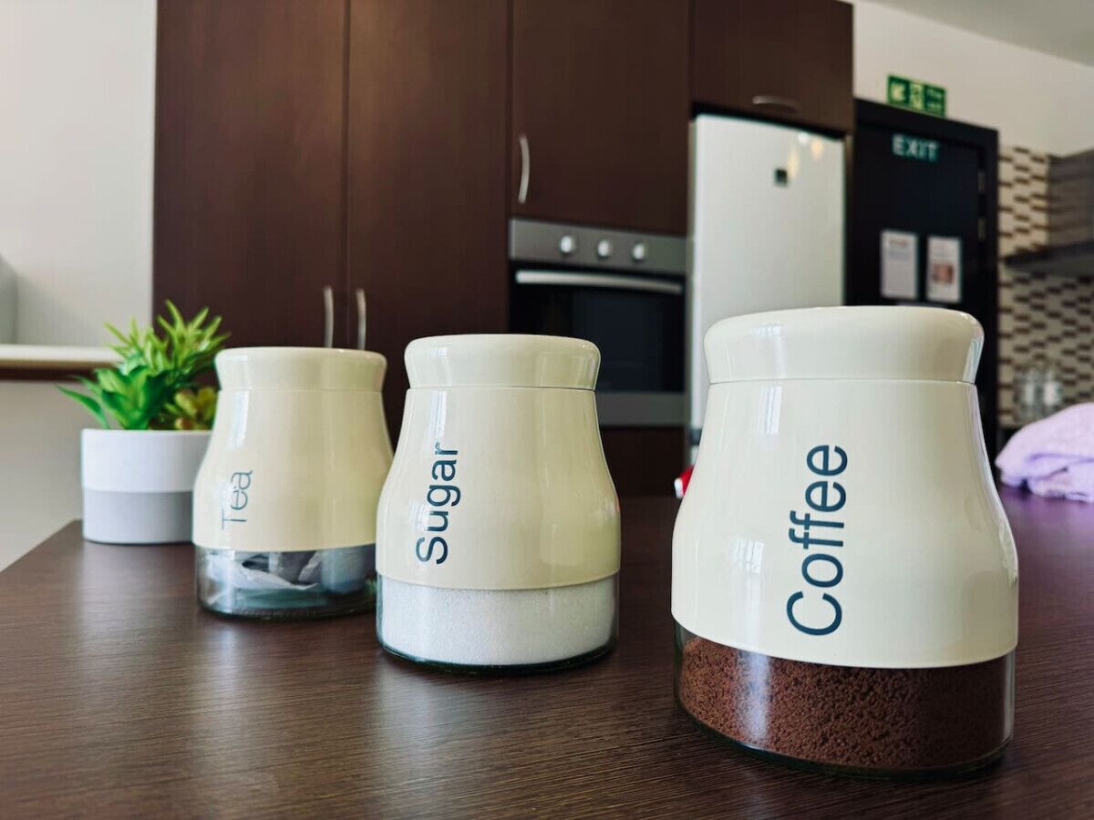 Drei Behälter mit den Aufschriften 'Tee', 'Zucker' und 'Kaffee' auf einem Holztisch in einer Küche.