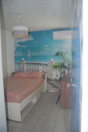 Ein Schlafzimmer mit Bett, einer Wandmalerei mit Strandmotiv, einer Deckenleuchte und einem Fenster.