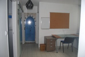 Ein Zimmer mit blauer Tür, einer Tafel, einem Schreibtisch mit Stuhl und einem Aktenschrank.