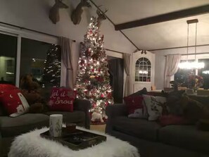 Una sala de estar acogedora con un árbol de Navidad decorado, una chimenea y un amplio ventanal.