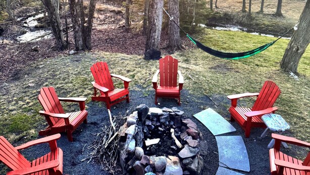A fire pit surrounded by red Adirondack chairs, a hammock, and a view of a sunset over a lake. - Beach by the Lake -Cozy Stay with Gorgeous Views (Pocono lake)
