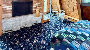 A rustic room with a brick fireplace, a wooden ceiling, and a patterned carpet. - Rustic Pine Lodge - Cozy 4 BR Adirondack Escape (Schroon Lake)