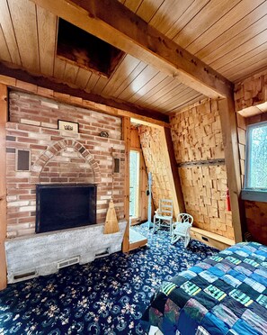 Una habitación rústica con chimenea de ladrillo, techo de madera y alfombra estampada.